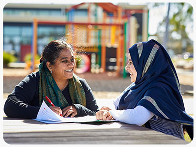 An adult and a child sitting at an outdoor table, engaged in conversation