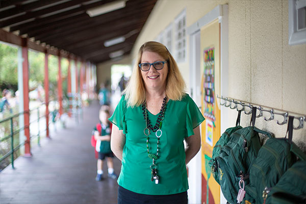 An educator outside a school, smiling at the camera