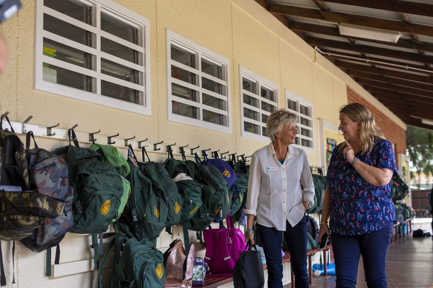 Two adults walking outside a school, engaged in conversation 