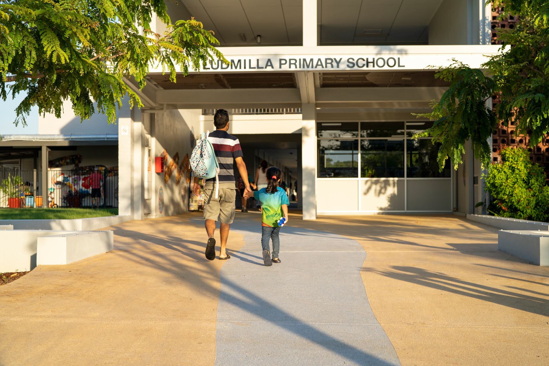 An adult and child, walking hand in hand towards a school