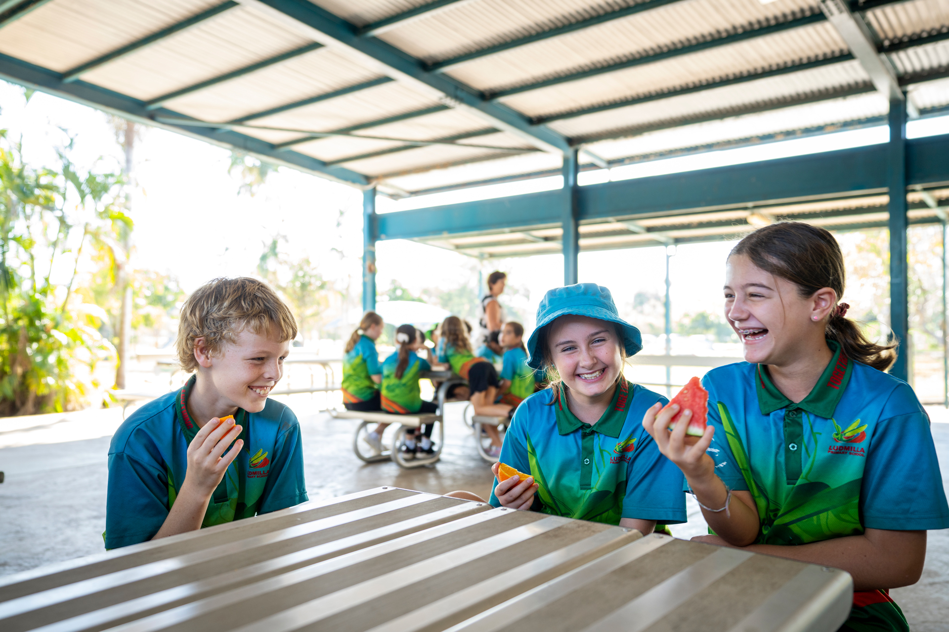 Three children sitting at a table, eating watermelon and laughing 