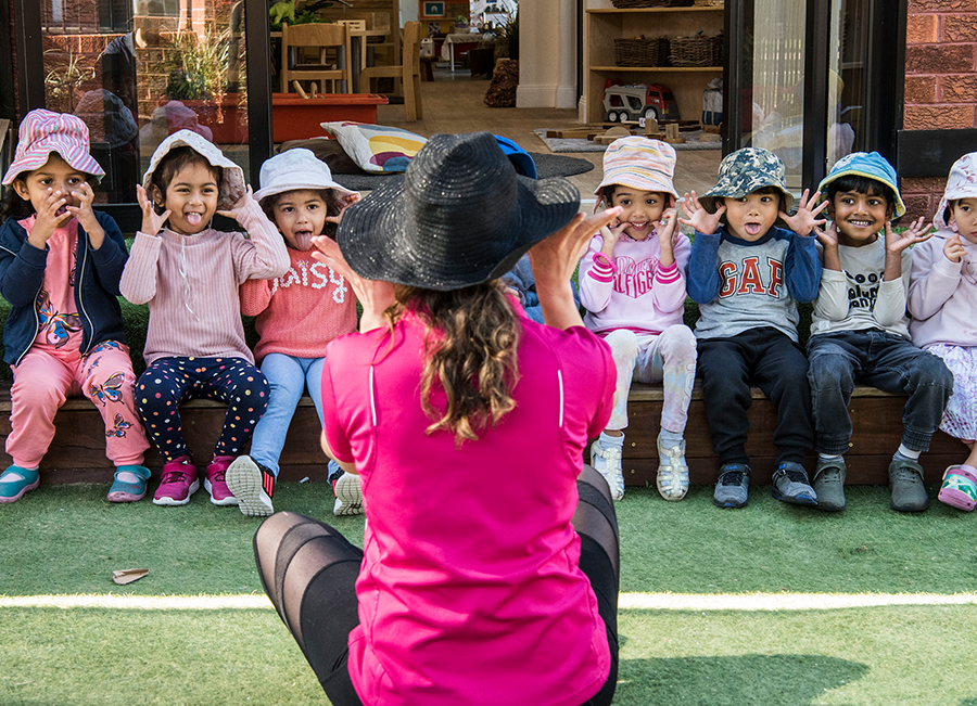 Photo of educator sitting on ground teaching children in a row.