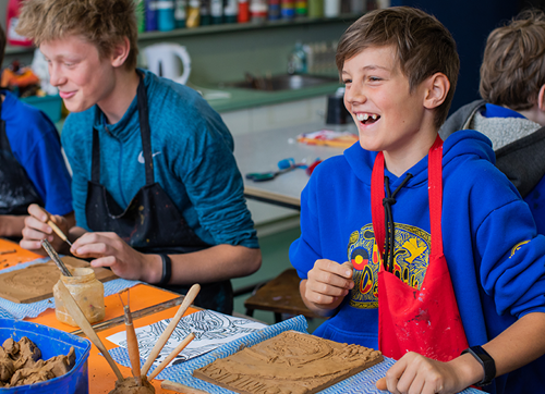 Photo of young child making clay sculpture and laughing with school mates.