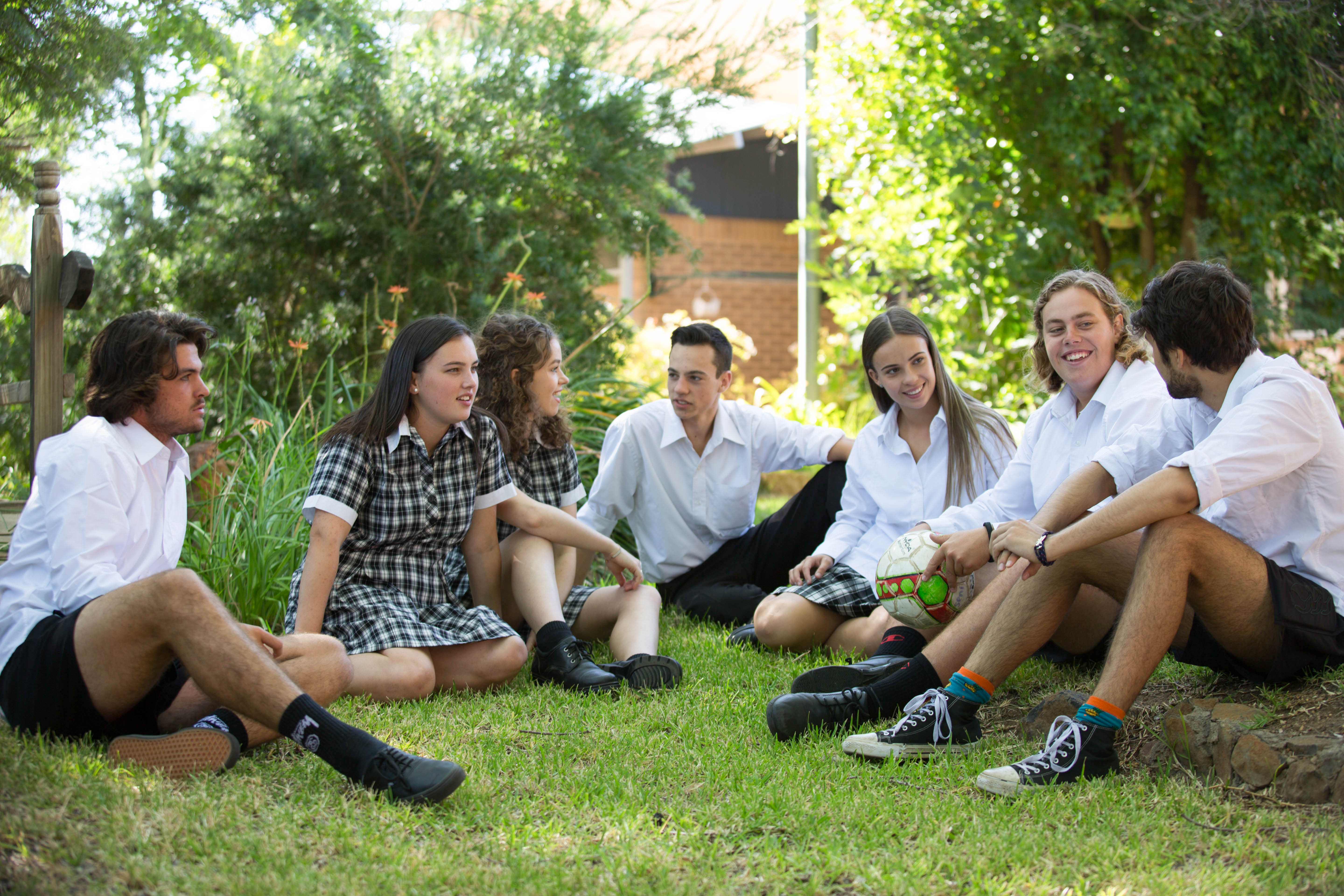 A group of teenagers sitting outside on grass, engaged in conversation