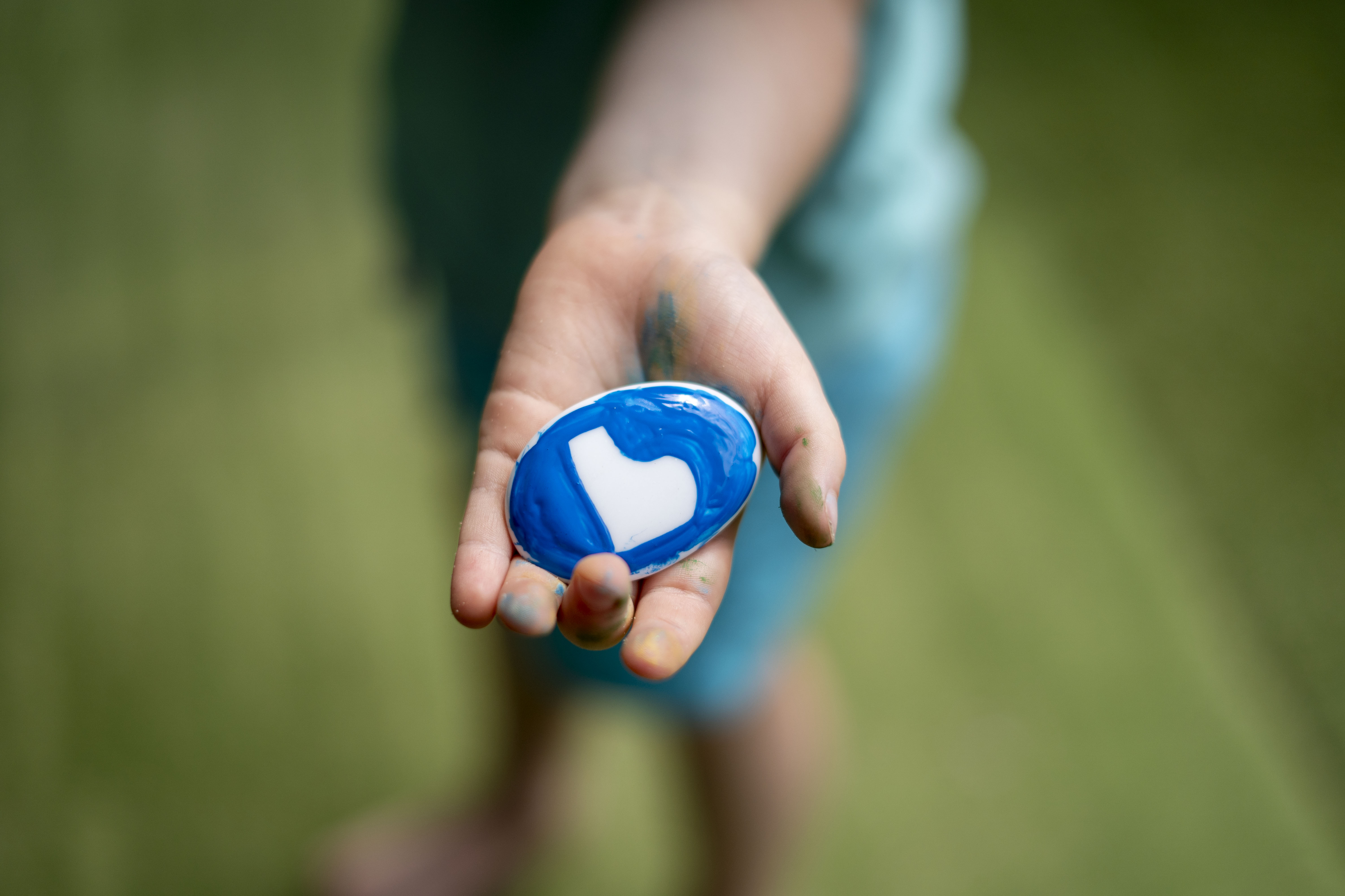 A child's hand holding a rock that has been painted blue with a white letter b in the centre.