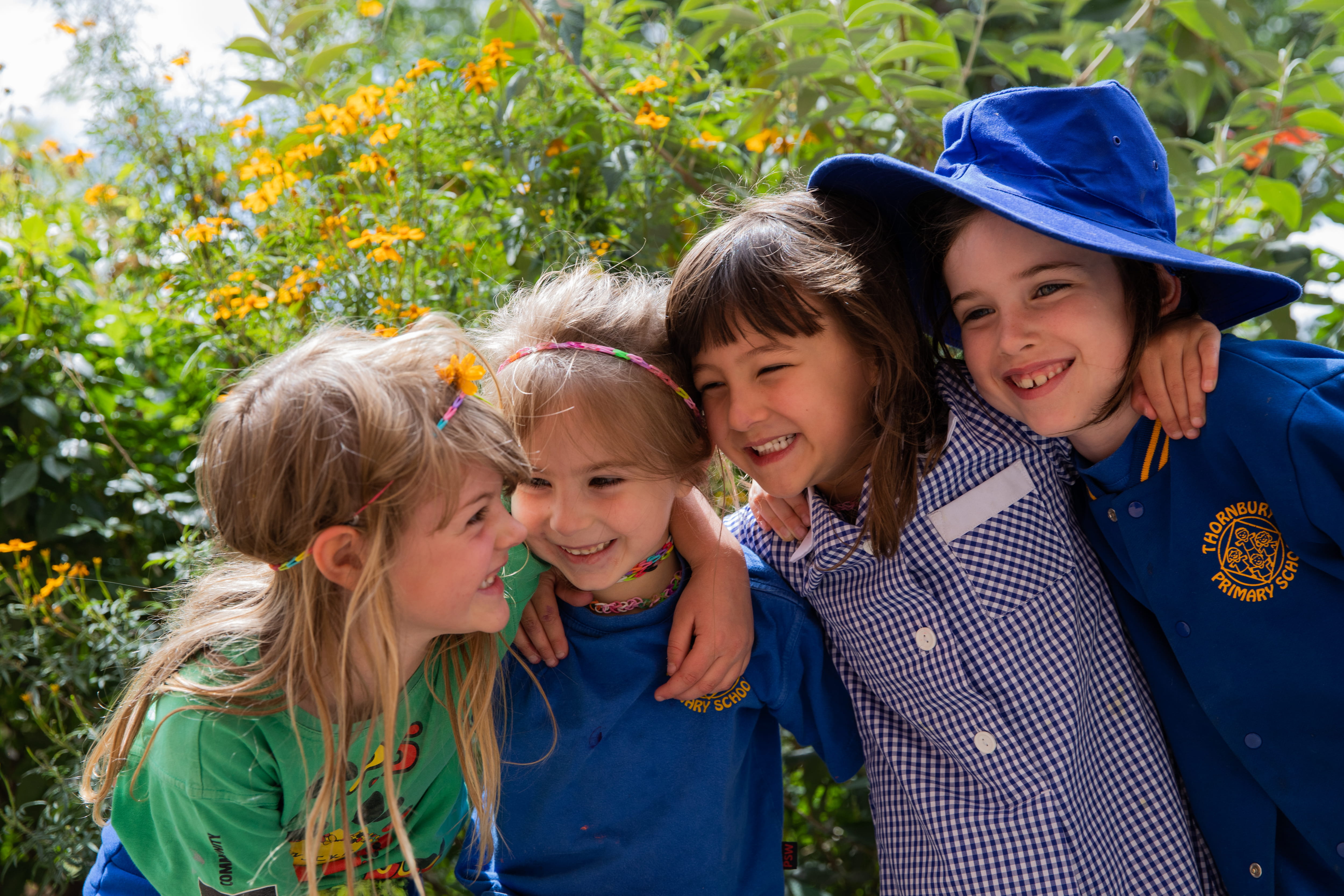 Four young school children standing in a line with their arms around each other's shoulders smiling.